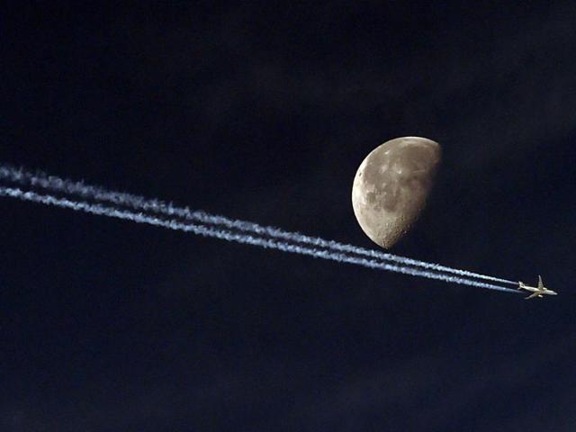 A jetliner leave a vapour trail as it passes in front of the moon taken from the Algerian capital Algiers. (AFP photo)