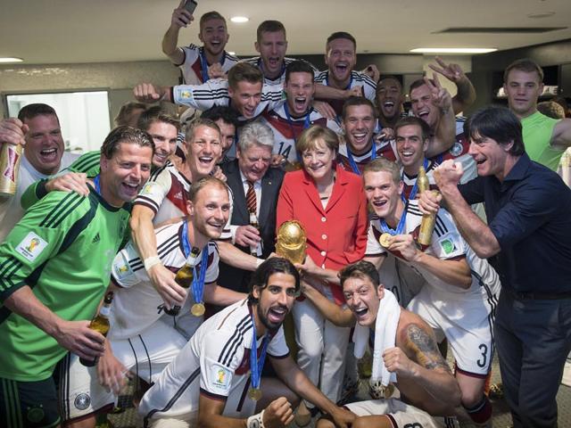 German chancellor Angela Merkel, center right, and German president Joachim Gauck, center left, pose with the German soccer squad and the trophy in the changing room, after the Germans won against Argentina by 1-0 in the World Cup soccer final on July 13, 2014. At right, national soccer coach Joachim Loew. (AP Photo-Guido Bergmann, Bundesregierung)