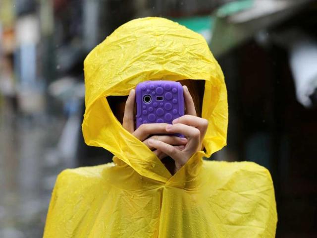 A Filipino resident takes pictures using her smartphone outside a flooded village as Typhoon Rammasun batters suburban Quezon city, north of Manila, Philippines. Typhoon Rammasun knocked out power in many areas but it spared the Philippine capital, Manila, and densely-populated northern provinces from being directly battered when its fierce wind shifted slightly away, officials said. (AP Photo/Aaron Favila)