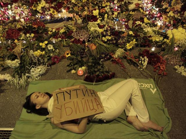 Ukrainian woman lies down in front of Dutch embassy holding a poster reading "Putin is a killer", in Kiev,Ukraine on July 17, 2014. A Malaysian Airlines passenger jet was shot down in eastern Ukraine on Thursday, and both the Ukrainian government and pro-Russian rebels blamed one another for the attack.(AP Photo/Sergei Chuzavkov)