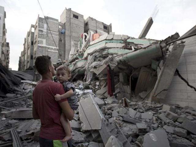 A Palestinian man carrying a child looks at the destroyed house of Hamas top leader Ismail Haniya, after it was hit by an overnight Israeli air strike on July 29, 2014 in Gaza City. (AFP/Mahmud Hams)