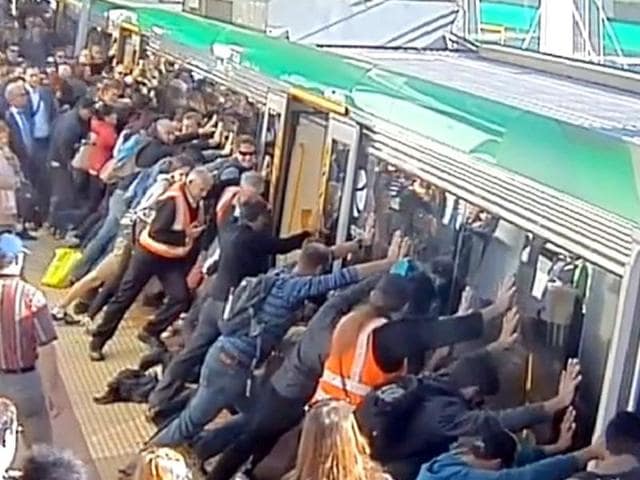 Commuters push a train to free a passenger's leg trapped between the train and the gap in Perth. (AFP Photo)