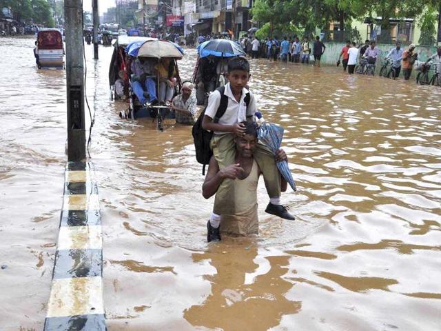 A man carries his child, wades through a waterlogged road after a heavy downpour at Chandmari in Guwahati. (PTI Photo)