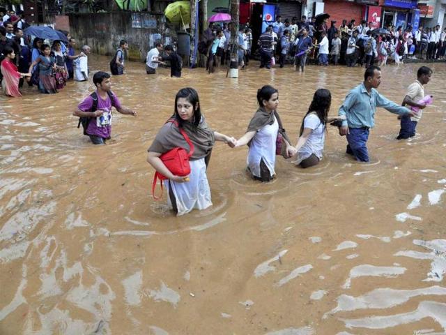 People holding each others hands to move across a waterlogged road at Chandmari in Guwahati after a heavy shower. (PTI Photo)