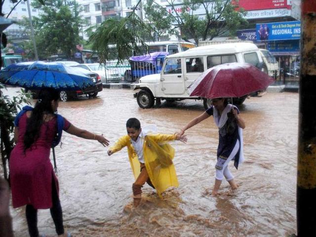 Parents with their children wade through a waterlogged GS Road after heavy showers in Guwahati. (PTI Photo)