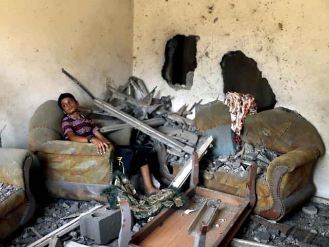 A Palestinian boy sits in his house, which witnesses said was damaged in an Israeli air strike, in Gaza City. (Reuters Photo)