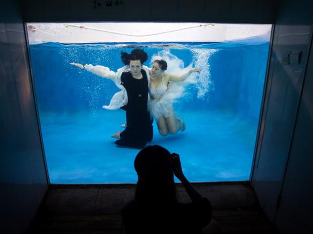 Qin Riyang (L) and Leng Yuting (C) pose underwater for their wedding pictures. Mr Wedding studio owner, Tina Lui, started providing underwater pictures four years ago. (AFP/Johannes Eisele)
