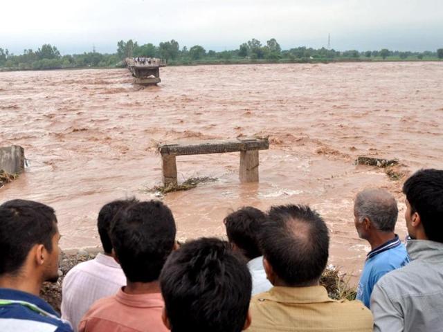Indian villagers look on at a missing section of a bridge across the overflowing Tawi river that was swept away as flooding continues in the Mandal area of Jammu. (AFP Photo)