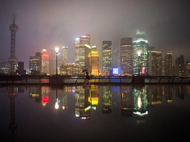 China, Shanghai: September 22, 2014 A woman walks through the rain in front of skyscrapers in Pudong, Shanghai. (AFP)