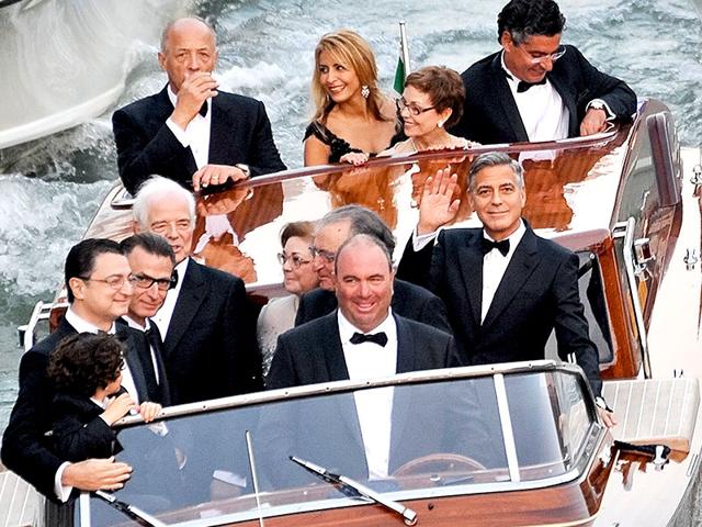 Actor George Clooney, right, waves from a boat with Ramzi Alamuddin, third from right front row, father of her fiancee Amal Alamuddin, his father Nick Clooney, fifth from right front row, and his mother Nina Bruce, second from right back row on their way to the Aman hotel ahead of his wedding in Venice, Italy. (AP)