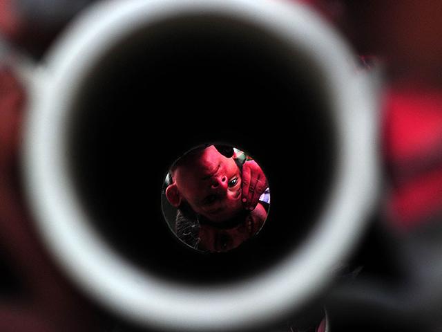 A vermillion seller peeps through cement pipes near Sangam in Allahabad. (AFP Photo/Sanjay Kanojia)