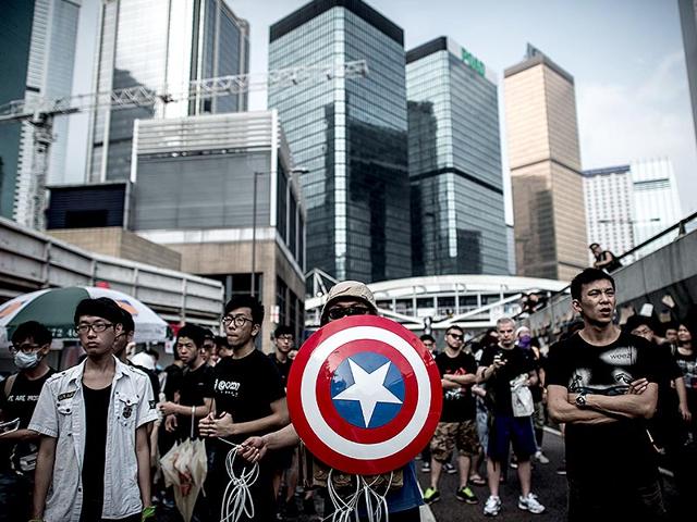Pro-democracy protesters, including one carrying a shield from the 'Captain America' comic book series stand their ground as they look out for the presence of rival protest groups next to a barricade on a road in Hong Kong. (AFP Photo/Philippe Lopez)
