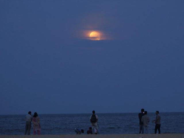 People watch the moon rise over the Bay of Bengal in Chennai. (AP Photo)