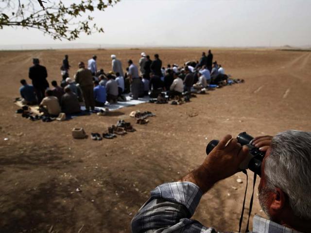 A Turkish Kurd uses binoculars to watch intensified fighting over the border in Kobani, Syria, between Syrian Kurds and the militants of Islamic State group, as Turkish Kurds offer their Muslim Friday prayers in support of Syrian Kurds. (AP Photo) 