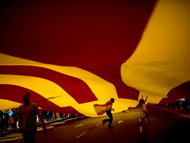 People walk under a huge Spanish flag as they celebrate the 'Dia de la Hispanidad' holiday or Spain's National Day in Barcelona. (AP Photo)
