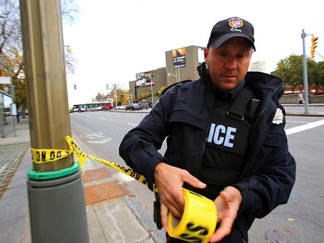 An Ottawa police officer puts up yellow tape at Elgin St. and Slater near the National War Memorial blocks away from Parliament Hill. (AFP Photo)