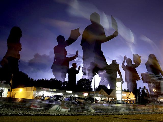 Protesters march in the street as lightning flashes in the distance in Ferguson. (AP Photo)