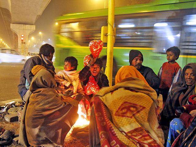 A family that migrated from Jaipur, Rajasthan, huddle around a fire on a cold winter night under a flyover near Rithala in north-west Delhi. (Subrata Biswas/HT Photo)