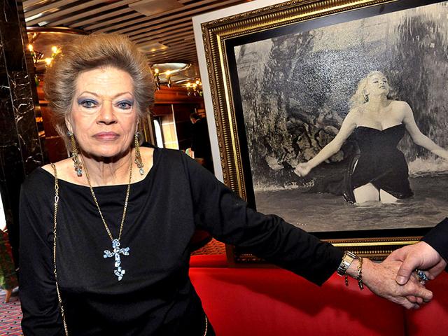 A picture taken on June 21, 2010 shows Swedish-born film star Anita Ekberg posing aboard the Italian cruise ship Costa Atlantica at quay in Stockholm next to a picture showing her famous swim in the Trevi fountain in La Dolce Vita by Italian director Federico Fellini in 1960. Anita Ekberg died near Rome, aged 83, media reports say on January 11, 2015. (AFP)