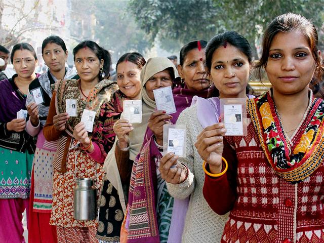 Women voters show their voter ID cards as they wait in a queue to cast their votes for the Delhi assembly elections at Pul Prahladpur. (PTI Photo)