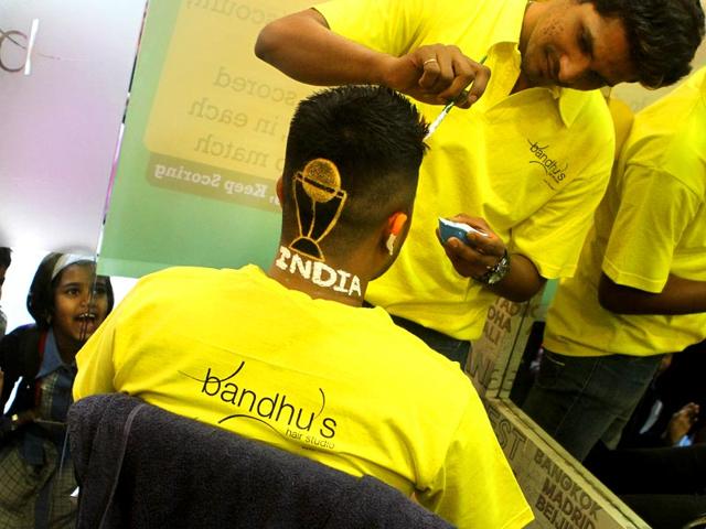 World Cup is nearing and Mumbai is gripped with cricket fever. School kids watch as a cricket fan gets the world cup trophy painted on his head. (Arijit Sen/HT photo)