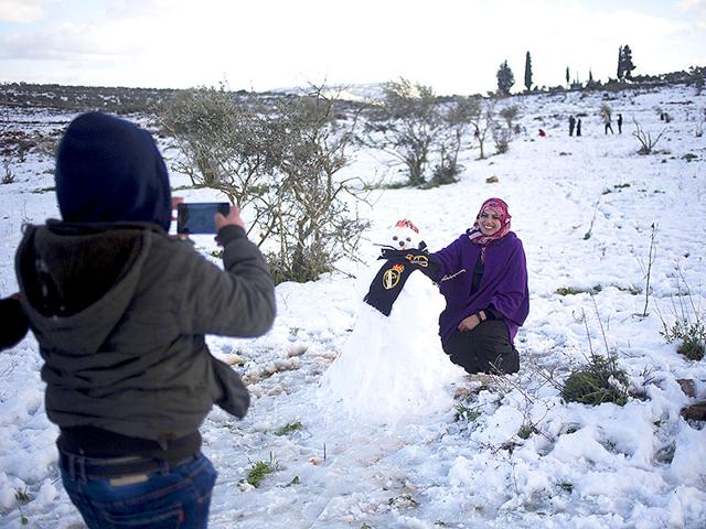 A Palestinian woman poses next to a snow man in Tapuah junction in the northern West Bank, near the Palestinian city of Nablus. (AP photo)