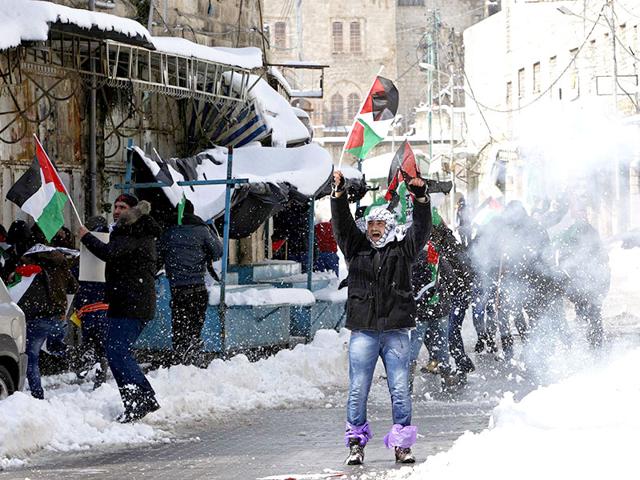 A Palestinian protester holding a Palestinian flag shouts anti-Israel slogans as snow scatters by a sound grenade thrown by Israeli soldiers during a demonstration against the closure of Shuhada street to Palestinians, in the West Bank city of Hebron. (Reuters)