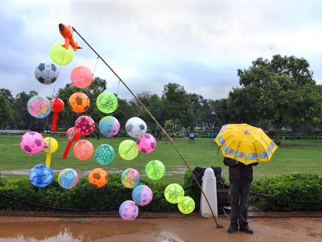 A toy seller takes shelter under an umbrela during rain near Raj Ghat in New Delhi. (HT photo/Subrata Biswas)