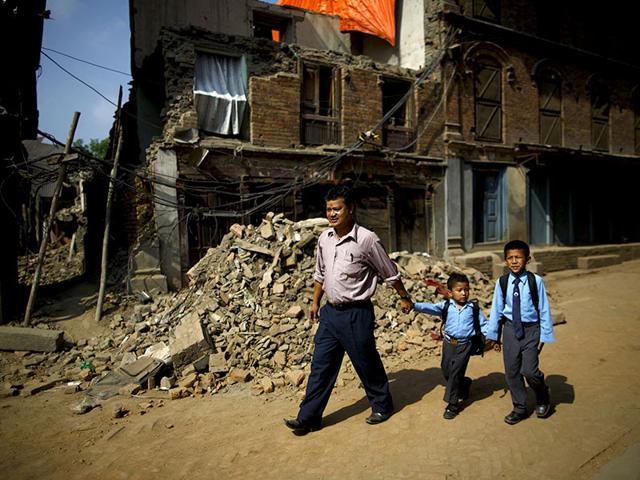 Birendra Karmacharya (L) walks past the debris of collapsed houses while holding the hand of his younger son Saksham Karmacharya, 4, along with his elder son Biyon Karmacharya (R), 9, as they head towards the school, a month after the April 25 earthquake in Bhaktapur. (Reuters)