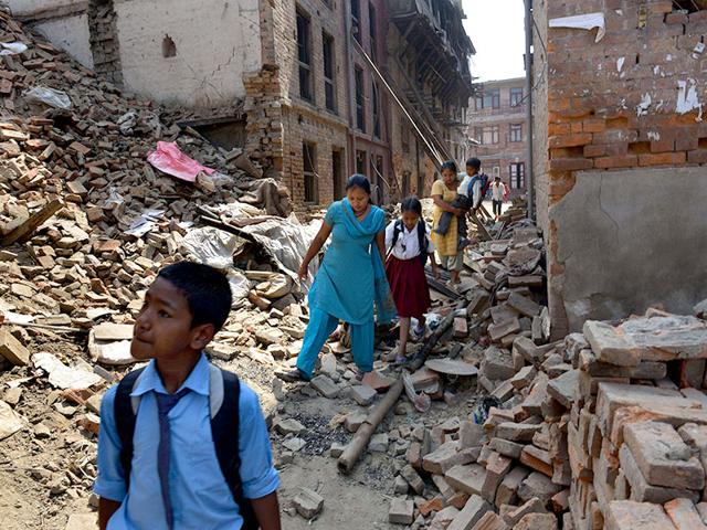 Nepalese parents walk with their children past damaged buildings to school in Bhaktapur. (AFP Photo)