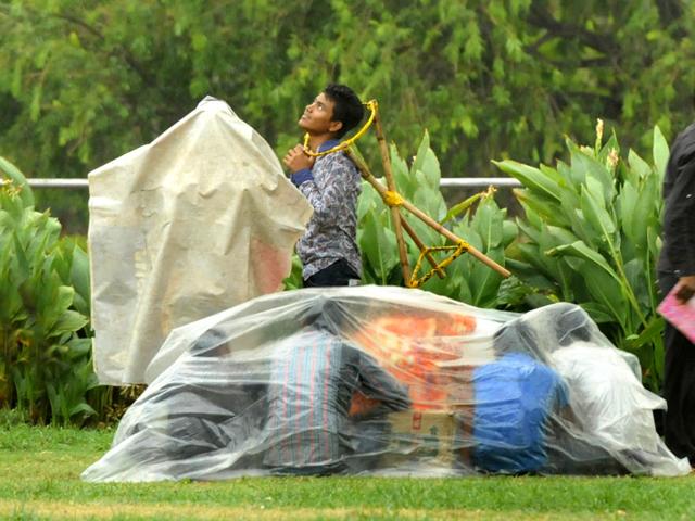 Road side hawkers use a plastic sheet to protect themeselves from rain following a dust storm at Rajpath in New Delhi. (Mohd Zakir/ HT Photo)