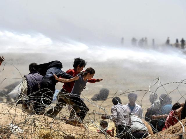Syrian refugees flee as Turkish soldiers use water cannons to move them away from fences at the Turkish border near the Syrian town of Tal Abyad (AFP Photo)