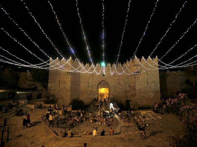 People walk under lights decorating Damascus Gate outside the old city of Jerusalem as Muslims around the world prepare for the announcement of the fasting month of Ramadan (AFP Photo)