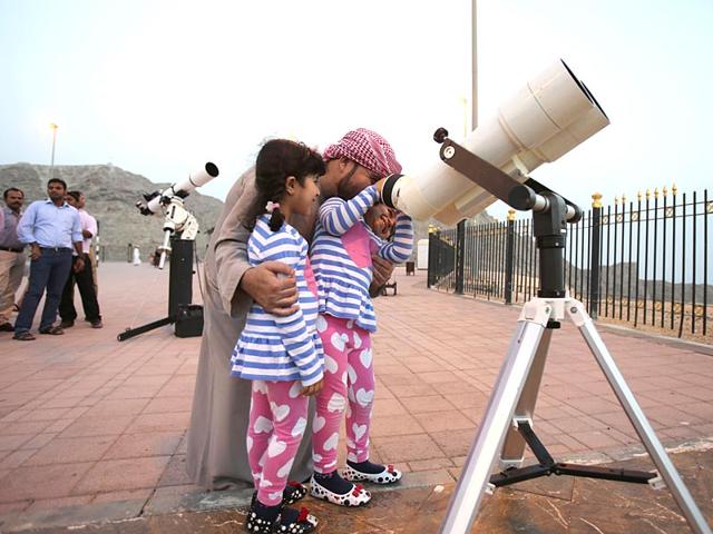 A father holds his girls as one of them looks into a telescope during a moon sighting event on top of Jebel Hafeet mountain ahead of the holy month of Ramadan (AP Photo)