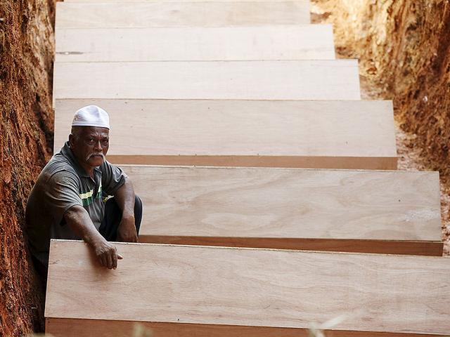 A man waits in a mass grave amongst coffins of unidentified remains of Rohingya people found at a traffickers camp (Reuters Photo)