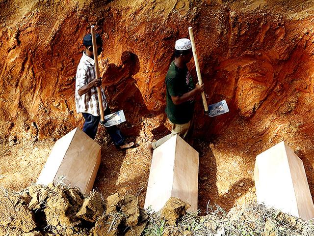 Workmen walk among coffins in a mass grave of unidentified Rohingya remains found at a traffickers camp last month (Reuters Photo)