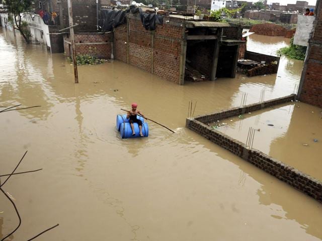 A man uses plastic drums to cross a street flooded with rainwater in New Sunder Nagar area of Indore on Wednesday. (Arun Mondhe/HT)