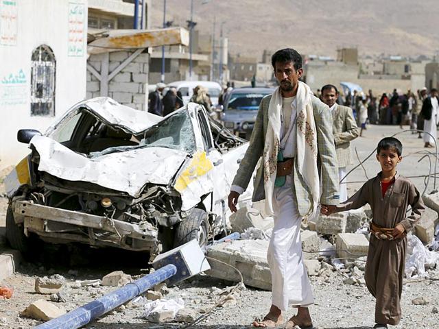 A man and his son walk past a car destroyed by Saudi-led air strikes on the nearby offices of the education ministry's workers union in Yemen's northwestern city of Amran (Reuters Photo)