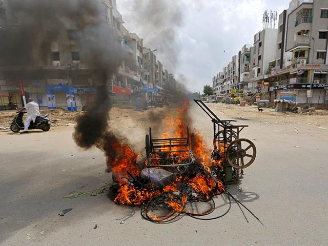 A man on a scooter stands next to burning vehicles after clashes between forces and protesters in Ahmedabad. The Patel community, led by Hardik Patel, has been demanding reservation for the powerful community. (Reuters Photo)