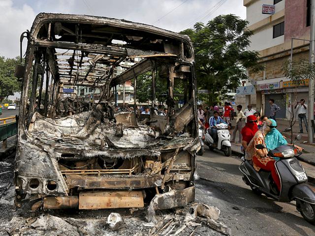 Commuters ride their motocycles next to the wreckage of a bus that was burnt during clashes between the police and protesters in Ahmedabad. (Reuters Photo)