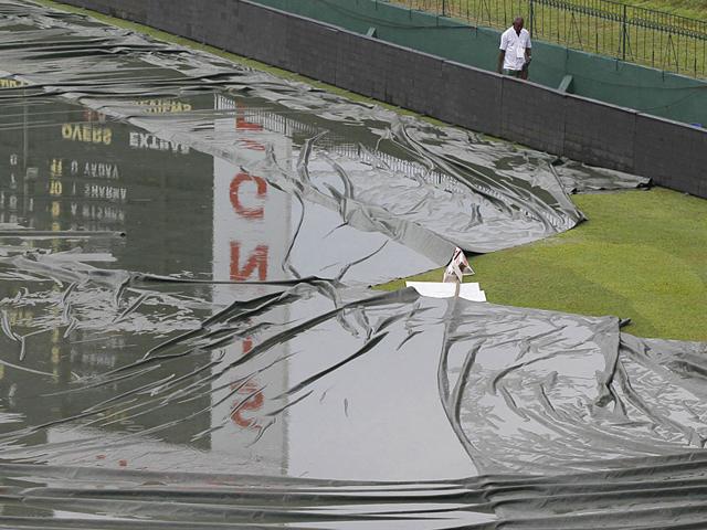 A ground staff member walks past the covered outfield following a spell of rain that washed out play for the day. (AP Photo) A ground staff member walks past the covered outfield following a spell of rain that washed out play for the day. (AP Photo)