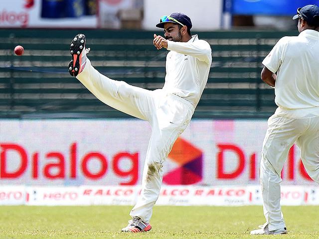 Indian Test captain Virat Kohli, left, kicks the ball in celebration after taking a catch to dismiss Perera. (AFP Photo)