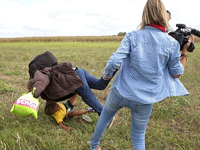 A migrant carrying a child falls after tripping on a TV camerawoman while trying to escape from a collection point in Roszke village, Hungary. (reuters) A migrant carrying a child falls after tripping on a TV camerawoman while trying to escape from a collection point in Roszke village, Hungary. (reuters)