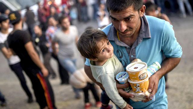 A Syrian man carries packaged food as he cradles his child in his arms as they rest beside the highway on their way to the border between Turkey and Greece in Edirne. (AFP) A Syrian man carries packaged food as he cradles his child in his arms as they rest beside the highway on their way to the border between Turkey and Greece in Edirne. (AFP)