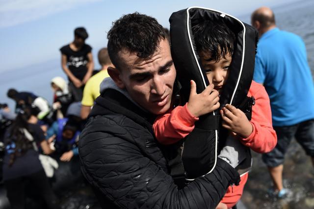 A man carries a child as he arrives with other refugees and migrants to the Greek island of Lesbos after crossing the Aegean sea from Turkey. (AFP Photo) A man carries a child as he arrives with other refugees and migrants to the Greek island of Lesbos after crossing the Aegean sea from Turkey. (AFP Photo)