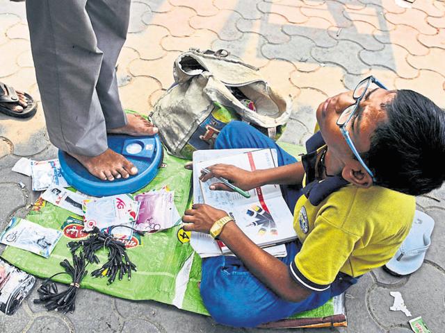 13-year-old, Harendra, sits outside Noida City Centre metro station with weighing scales and completes his homework while waiting for customers in Noida.(Sunil Ghosh/HT Photo)