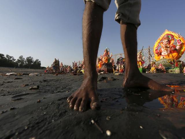 A worker pulling out idols from the polluted Yamuna river after their immersion on Monday. (Ravi Choudhary/ Hindustan Times)