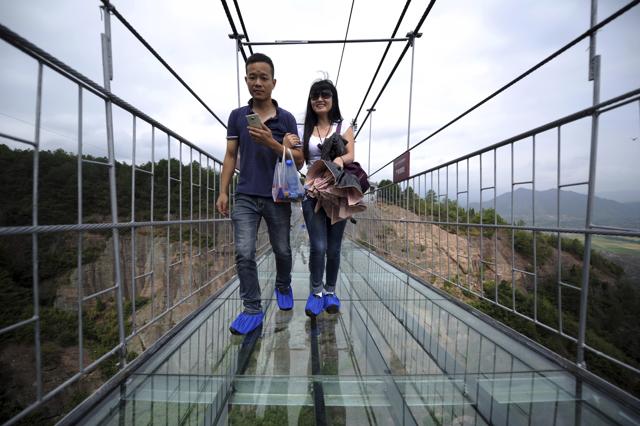 Visitors wear protective shoe coverings as they walk across a glass-bottomed suspension bridge. (AP)