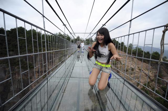 A woman plays around as she walks across a glass-bottomed suspension bridge. (AP)