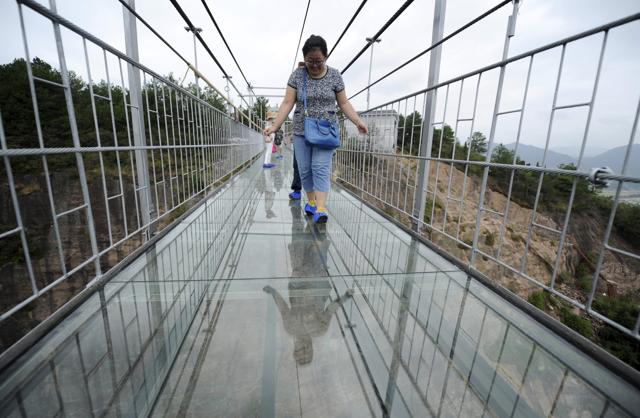 A tourist looks down as she walks on a glass suspension bridge. (REUTERS)